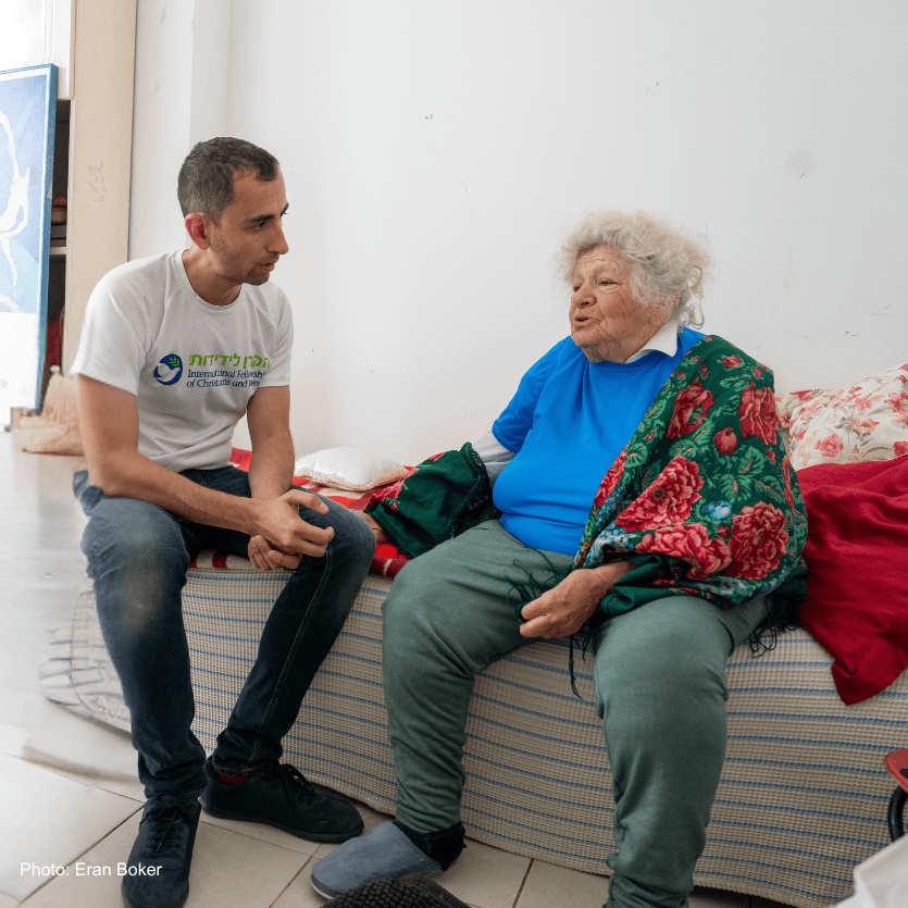 A young man providing compassionate support to an elderly woman in a care setting, highlighting kindness and community service.
