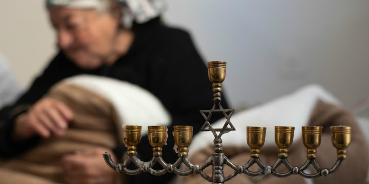Elderly Holocaust survivor sitting next to a small gold Menorah