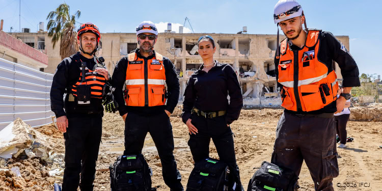 Emergency responders in orange vests and helmets working in a damaged urban environment.