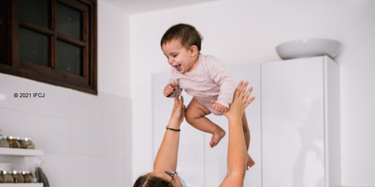Mother holding baby in the air against a white kitchen background.