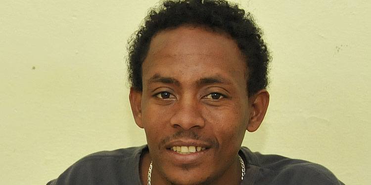 Man with curly hair, a silver chain, and gray shirt smiling into the camera.