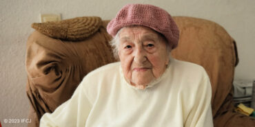 Elderly Jewish woman wearing a pink hat and white sweater.