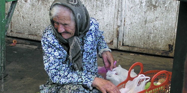 Elderly Jewish woman sitting on the ground rifling through an orange basket she has.