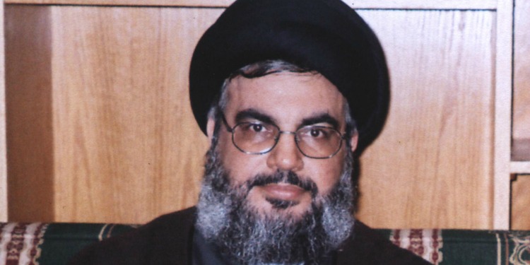 Sayyed Hassan sitting on a patterned couch against a wooden background.