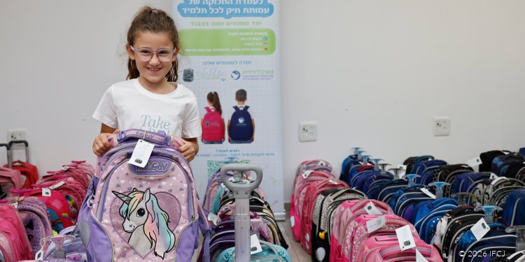 A young girl with glasses and a white T-shirt holding a purple unicorn backpack, surrounded by colorful backpacks for school supplies and vouchers.
