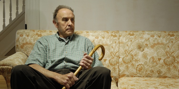 An elderly man sitting on a couch while holding his cane.