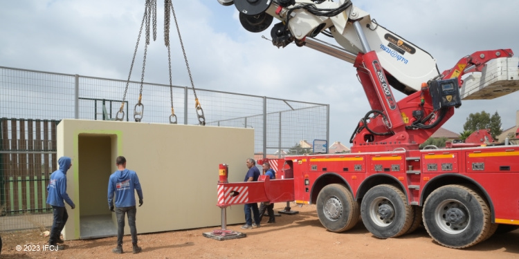 A red truck and four men working to build a bomb shelter near a soccer field.