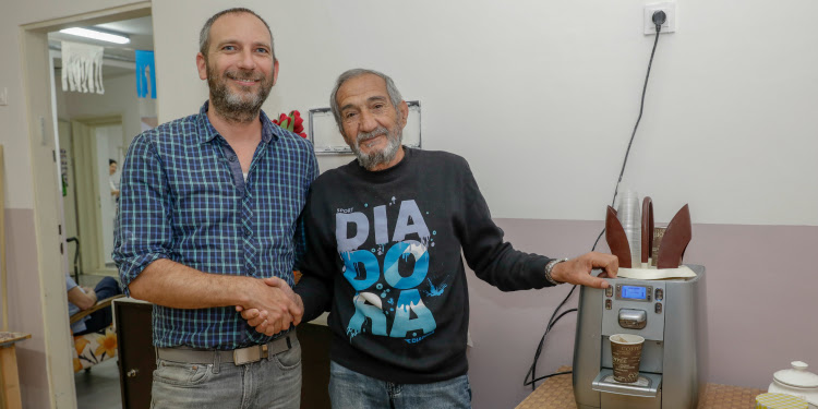 Two men shaking hands while standing next to a coffee machine.