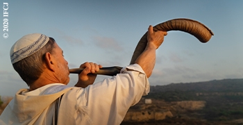 Man blowing a shofar at the top of a mountain.