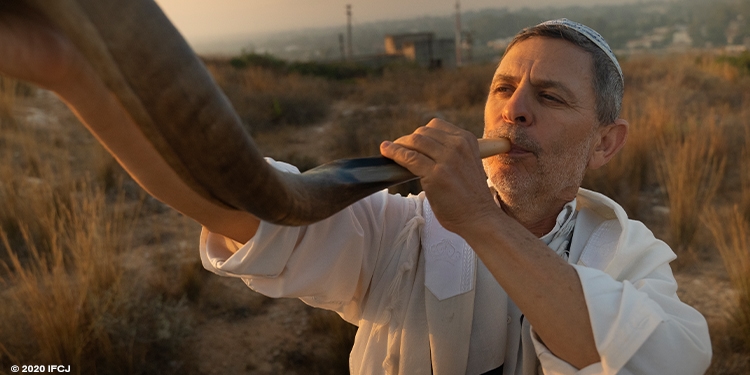 Close up image of a man in white blowing a shofar.
