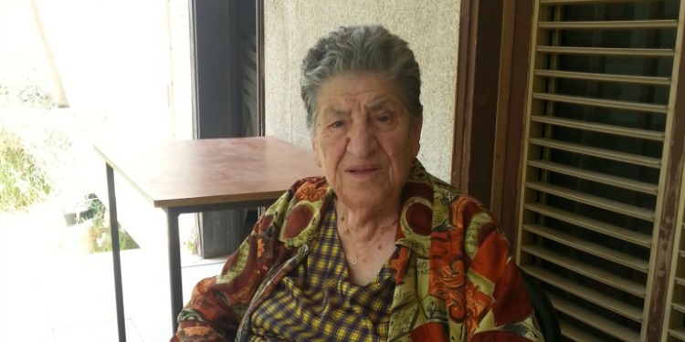 92-year-old woman in a green and orange top staring directly into the camera.