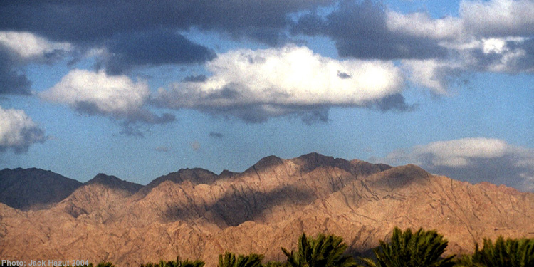 Mountains with palm trees in front of them and clouds overhead.