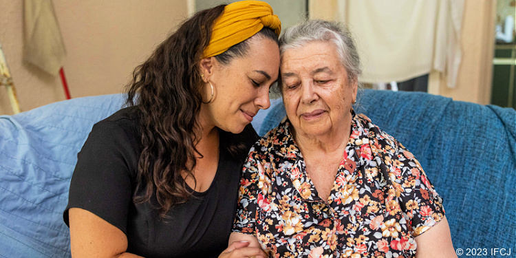 Yael Eckstein embraces elderly Jewish woman in floral shirt.