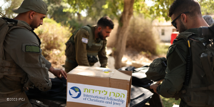 Three soldiers talking around a table with an IFCJ box on top of it.