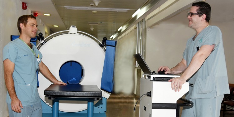 Two male nurses facing each other with a mobile CT scanner behind them.