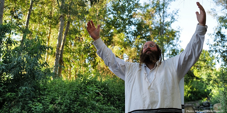 A man holding his hands up in the air in prayer while standing in the middle of the forest.