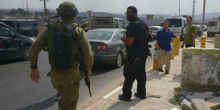 IDF soldier walking towards a car with three civilians beside it.
