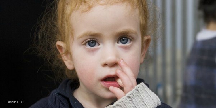 A young girl with red hair and blue eyes looking upwards.