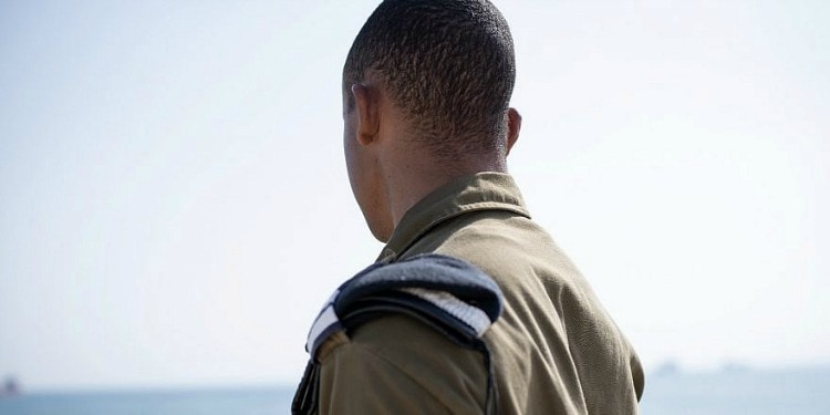 The back of a soldier looking out at water.