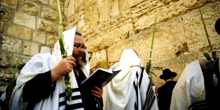 Men in robes reading scripture at the Western Wall.