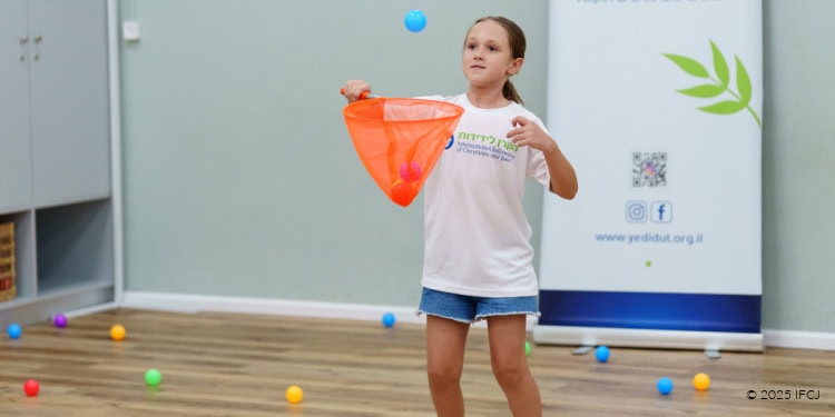 Young girl participating in summer activities for Olim children, tossing a ball into a net during a playful outdoor event.