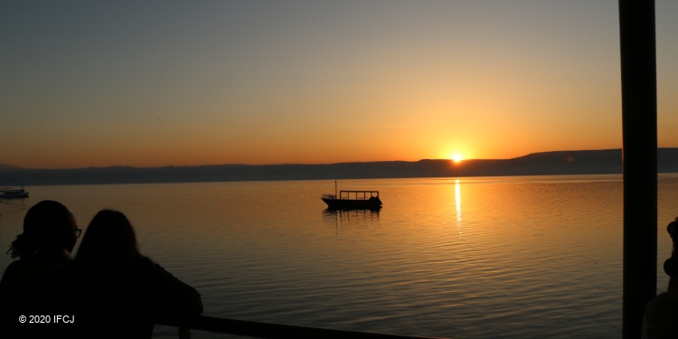 The sun rising over the Sea of Galilee as a single boat is in the water.