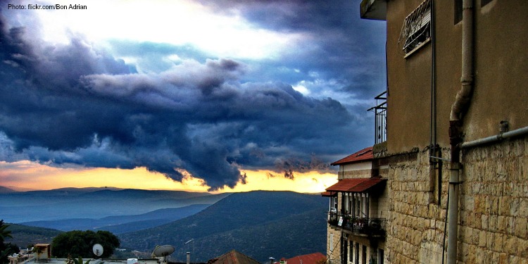 The side of a brick house with dark clouds coming over the mountains in front of it.