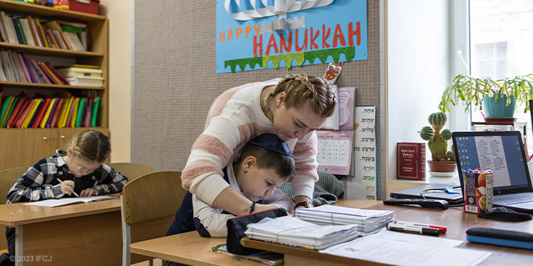 Teacher leaning over a student to help him with an assignment