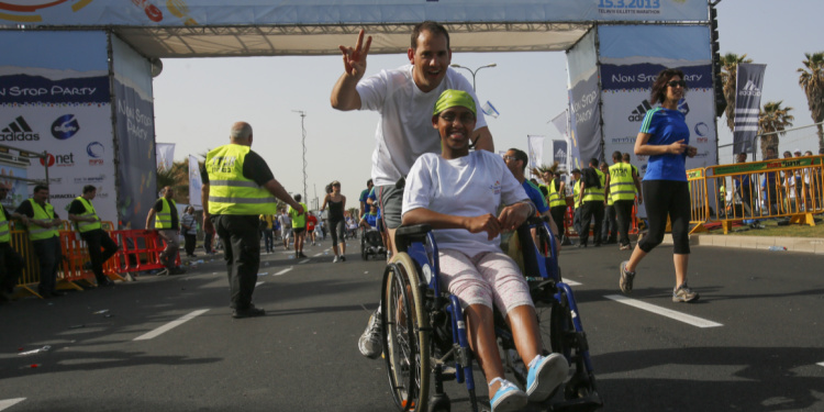 Person in a wheelchair being pushed by another person during a marathon.