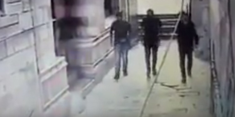 Three men walking out of a building on to a sidewalk.