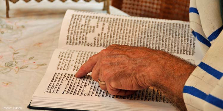 A devout man wearing a prayer shawl points to the Torah, the Word of God.