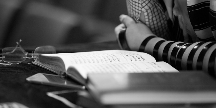 Black and white image of a person reading a book with Jewish writing.