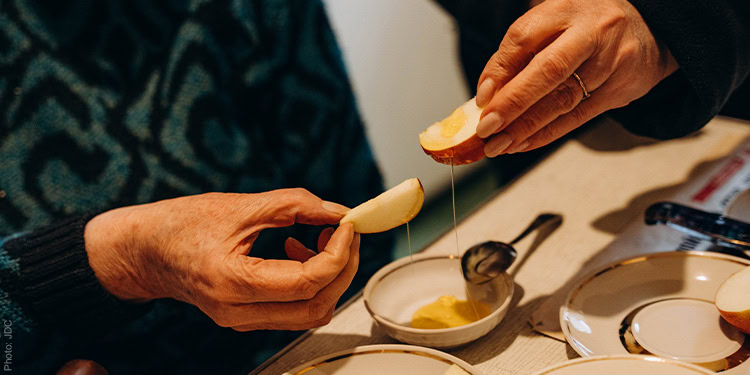 Two pairs of hands holding apples and dipping in honey