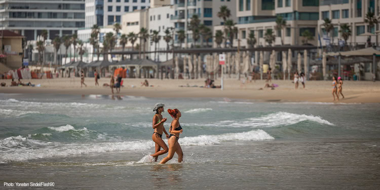 Two women running along the beach wearing bikinis