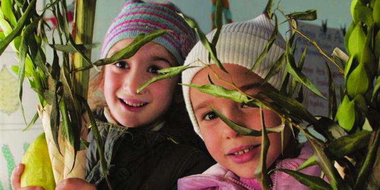 Two young girls hiding behind greenery while smiling at the camera.