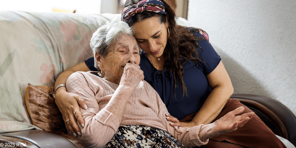 A young woman provides emotional support and comfort to an elderly woman sitting on a sofa, highlighting compassion and caregiving.