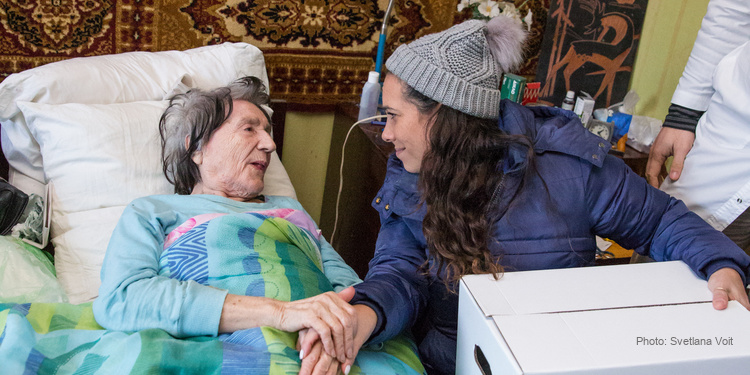 Yael Eckstein sitting near bed of bedridden elderly woman.