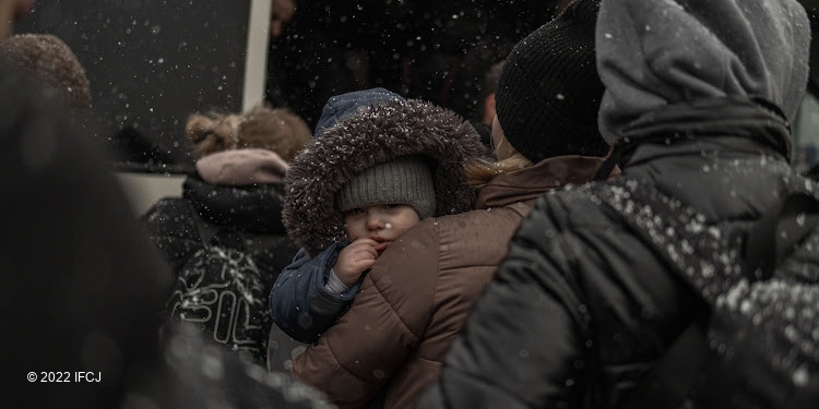 Young child facing the camera while his mother holds him during the wintertime.