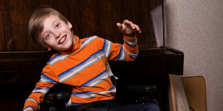 Young boy in orange shirt smiling at the camera.