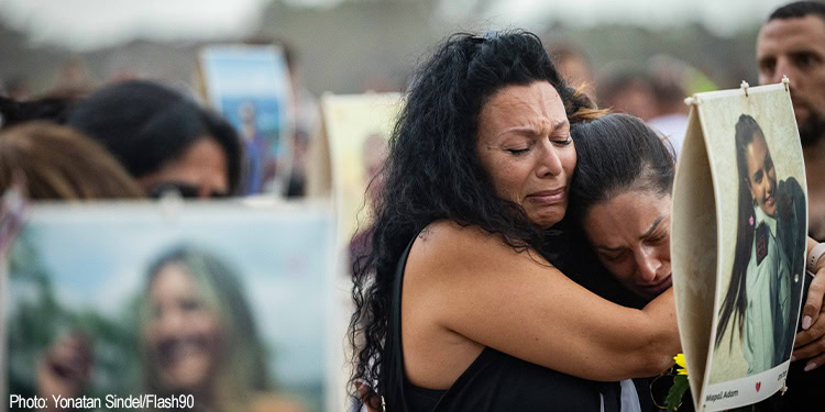 Victims of the Nova music festival holding signs and comforting each other