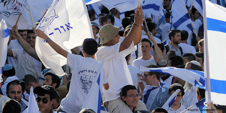 Several men gathered together celebrating while holding the Israeli flag.