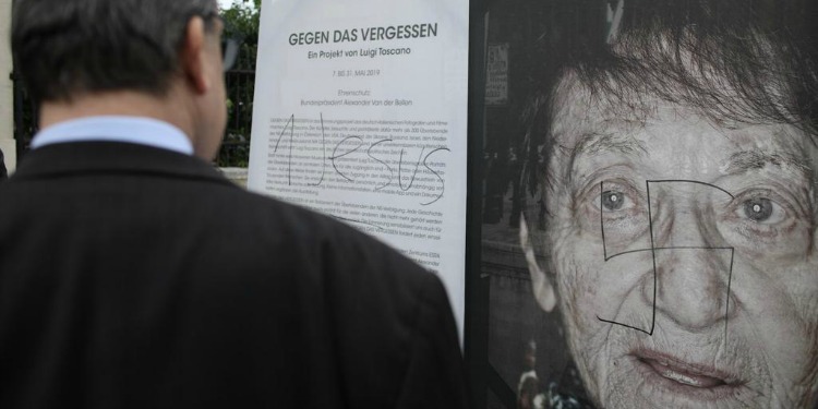 A man looking at a poster with a woman's story on it with a graffitied swastika on it.