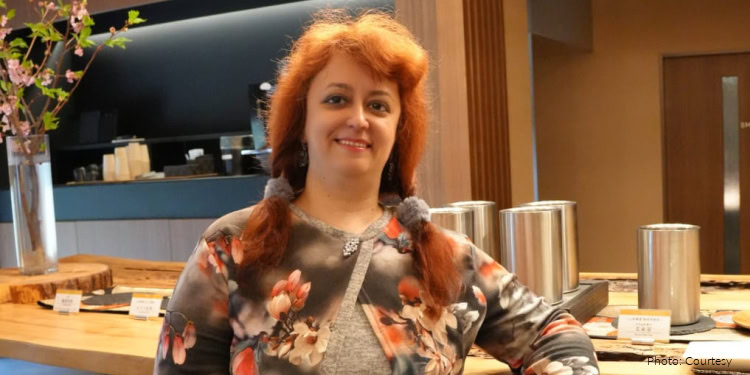 Viktoriia Voloshuk - Ukraine Aliyah - IFCJ-Canada - Fellowship Freedom Flight - April 30, 2026 woman with red hair, sitting at a table in a restaurant, smiling at camera - gray jacket with pink flowers