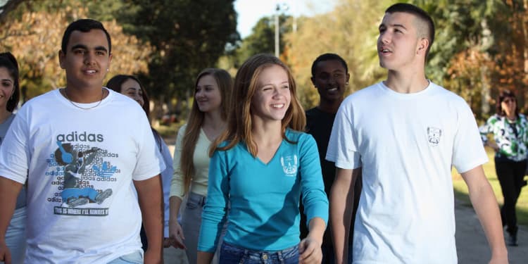 Two young men and a young woman walking with a few other peers behind them.