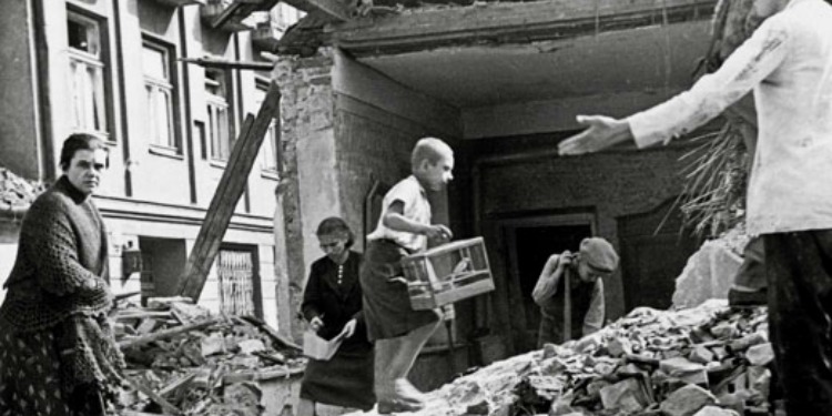 Black and white image of several gathering pieces of their home from a bombing.