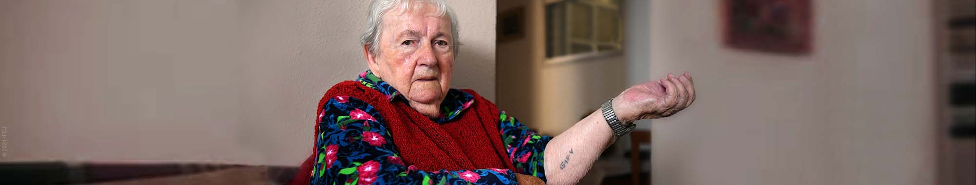 Elderly holocaust survivor sitting and showing her tattoo