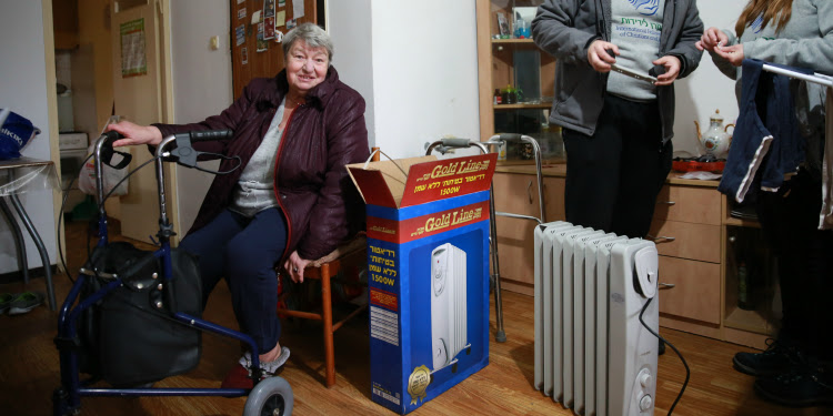 Svetlana Goligos sitting down next to her new heater with two IFCJ members behind her.