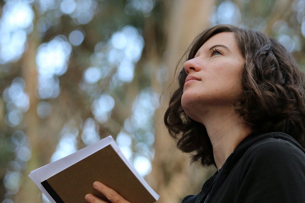 Woman holding book while looking up into the sky.