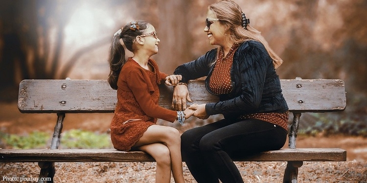 A mother and daughter smiling while sitting on a bench