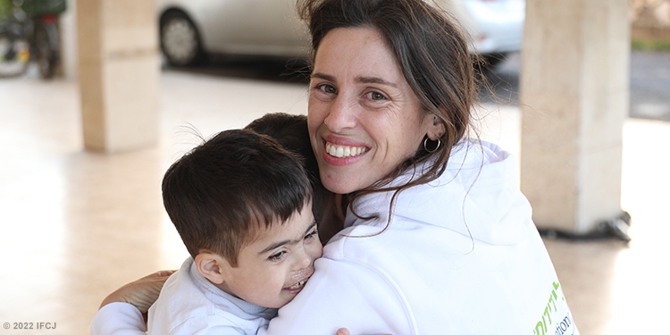 Woman smiling at the camera while embracing her two children.